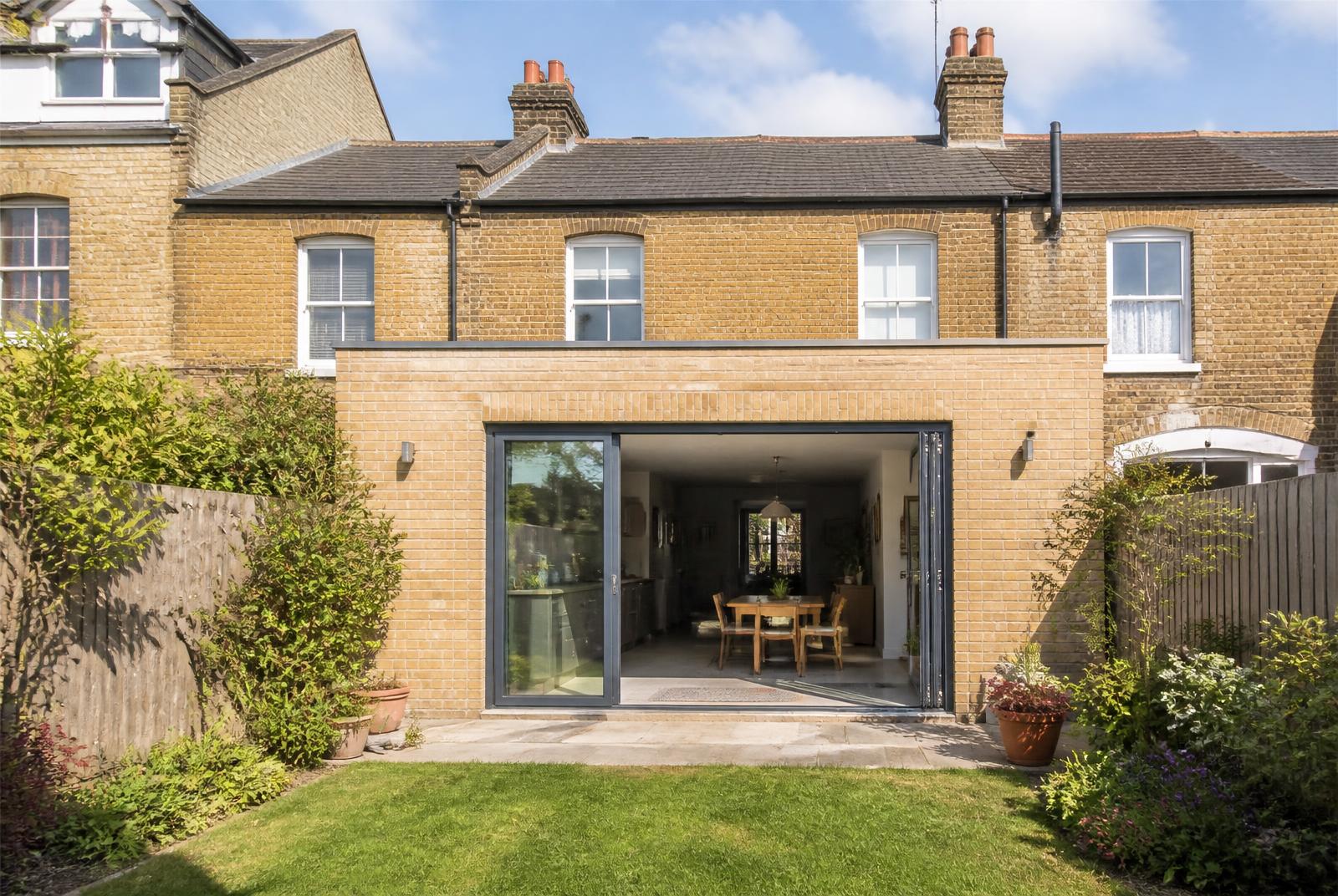 Rear of a Victorian terrace in Leigh on Sea with a new stock brick extension and wide sliding doors open to the garden on a sunny day
