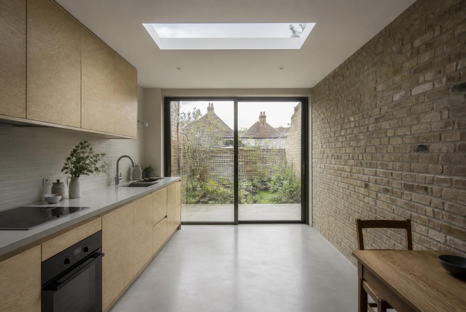 Kitchen in a new rear extension with a long island, pale joinery and daylight from a rooflight above the retained brick wall